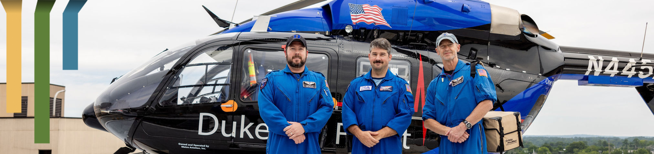 Three male team members smile in Duke Health Life Flight suits in front of a helicopter.