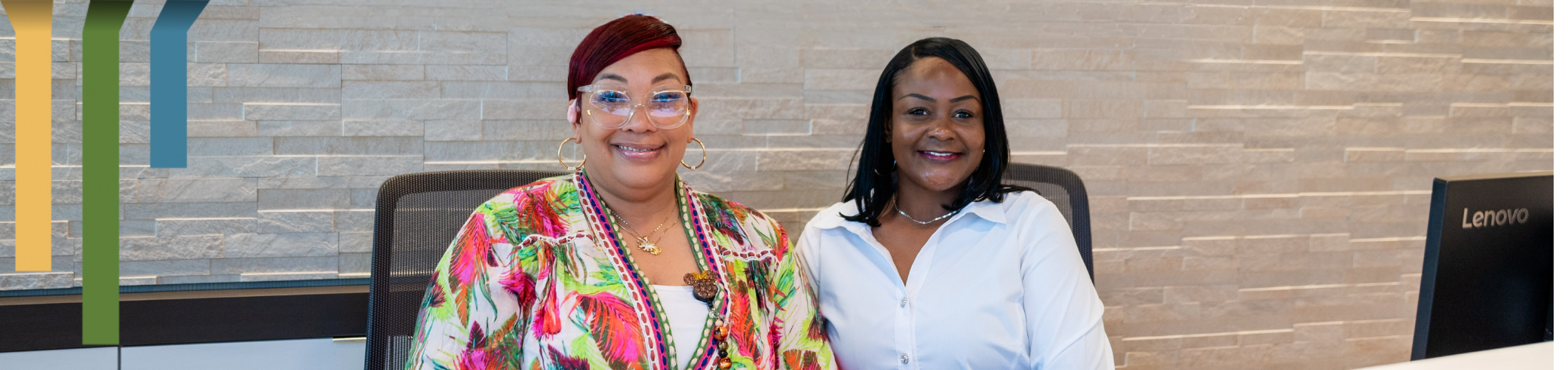 Two female team members smile by their computers.