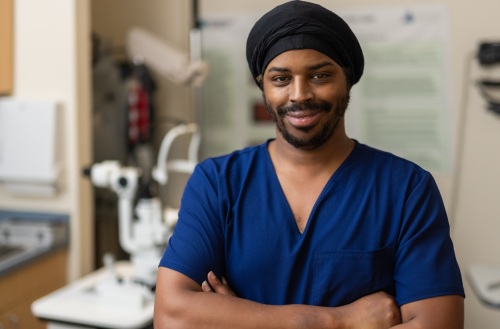 Male team member smiles in blue scrubs by eye machine.