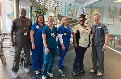 Team members in scrubs and business casual attire smile in a lobby together.