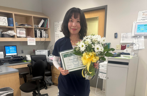 Nurse holds Daisy bouquet and award.