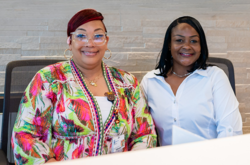 Two female team members smile together by their computers.