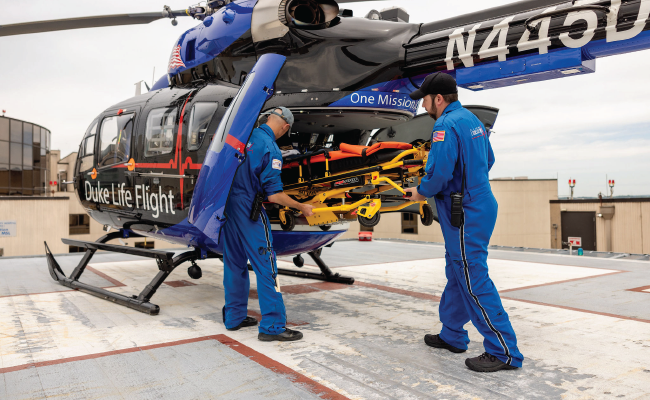 Two male team members remove equipment from a Duke Life Flight helicopter.