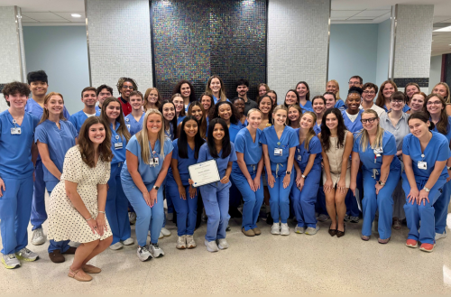 The 2025 cohort of PNAs smiles together in scrubs at graduation.