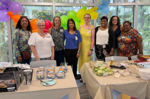 Team members smile together among balloons and food.