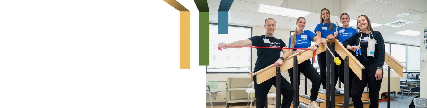 Five team members smile with rehab equipment in the gym at Duke Raleigh.