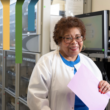 Female team member smiles in a white coat holding a piece of paper.