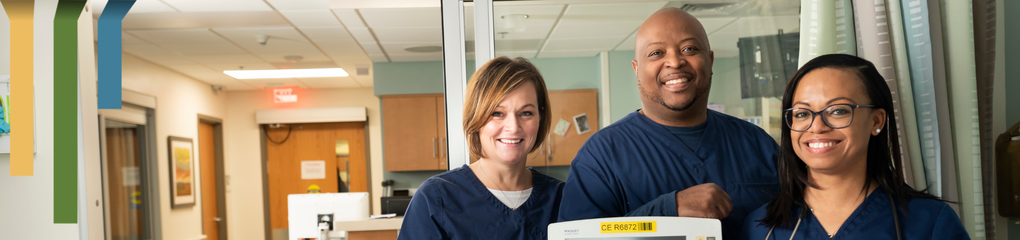 Three RTs smile together in blue scrubs by a machine.