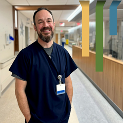 Male respiratory therapist smiles in blue scrubs in a Duke hospital hallway.