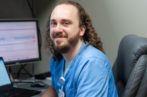 Male team member smiles in blue scrubs. 