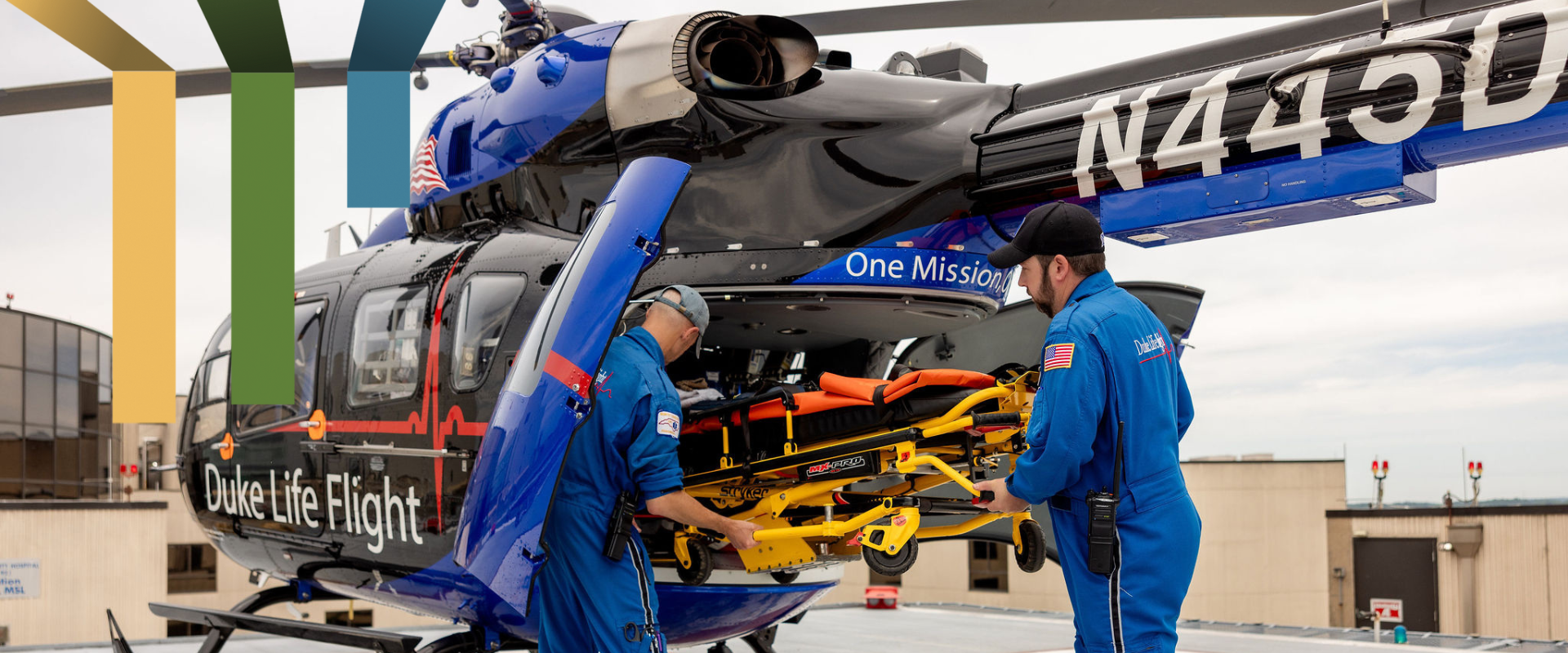 Two male team members load a stretcher into a helicopter.