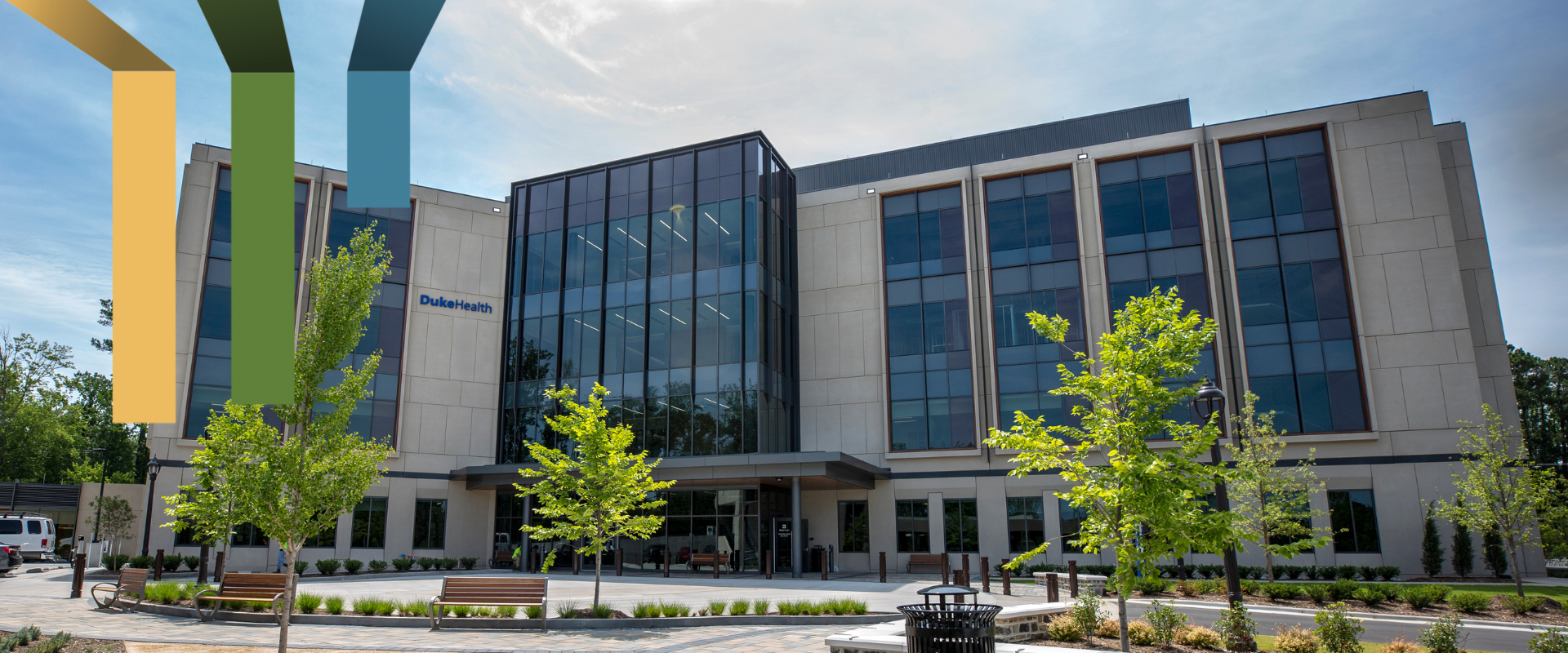 A clinic building with green trees and benches in the foreground.