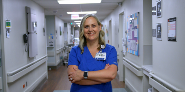 Joni smiles in blue scrubs in a Duke Regional Hospital hallway.