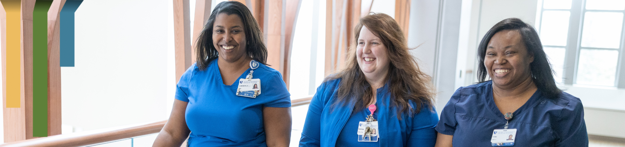 Three nurses smile as they walk down a clinic hallway.