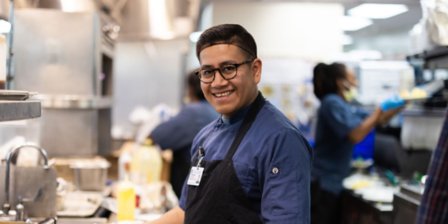 Food service team member smiles by grill in apron.