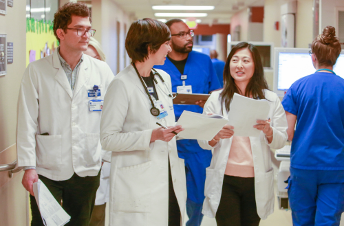 Team members smile together as they walk down a hospital hallway.