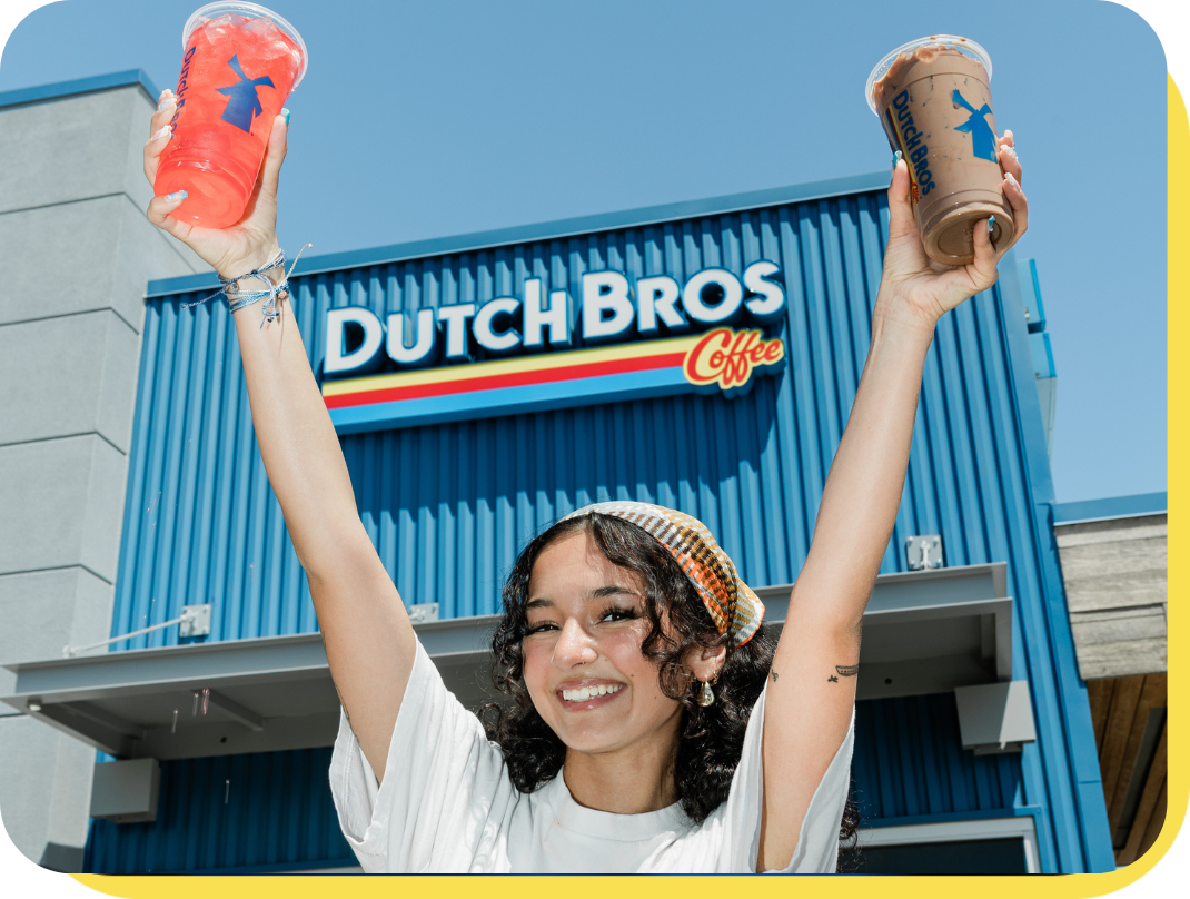 Brosita holding up two drinks outside of a shop