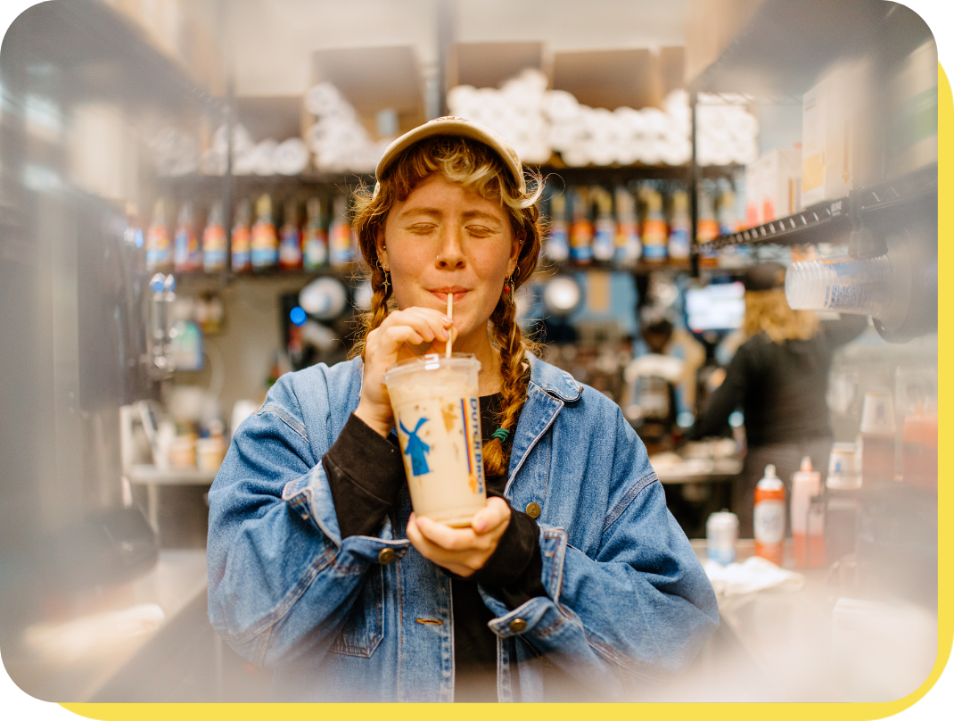 Person in braids and a hat drinking a dutch bros coffee through a straw and smiling
