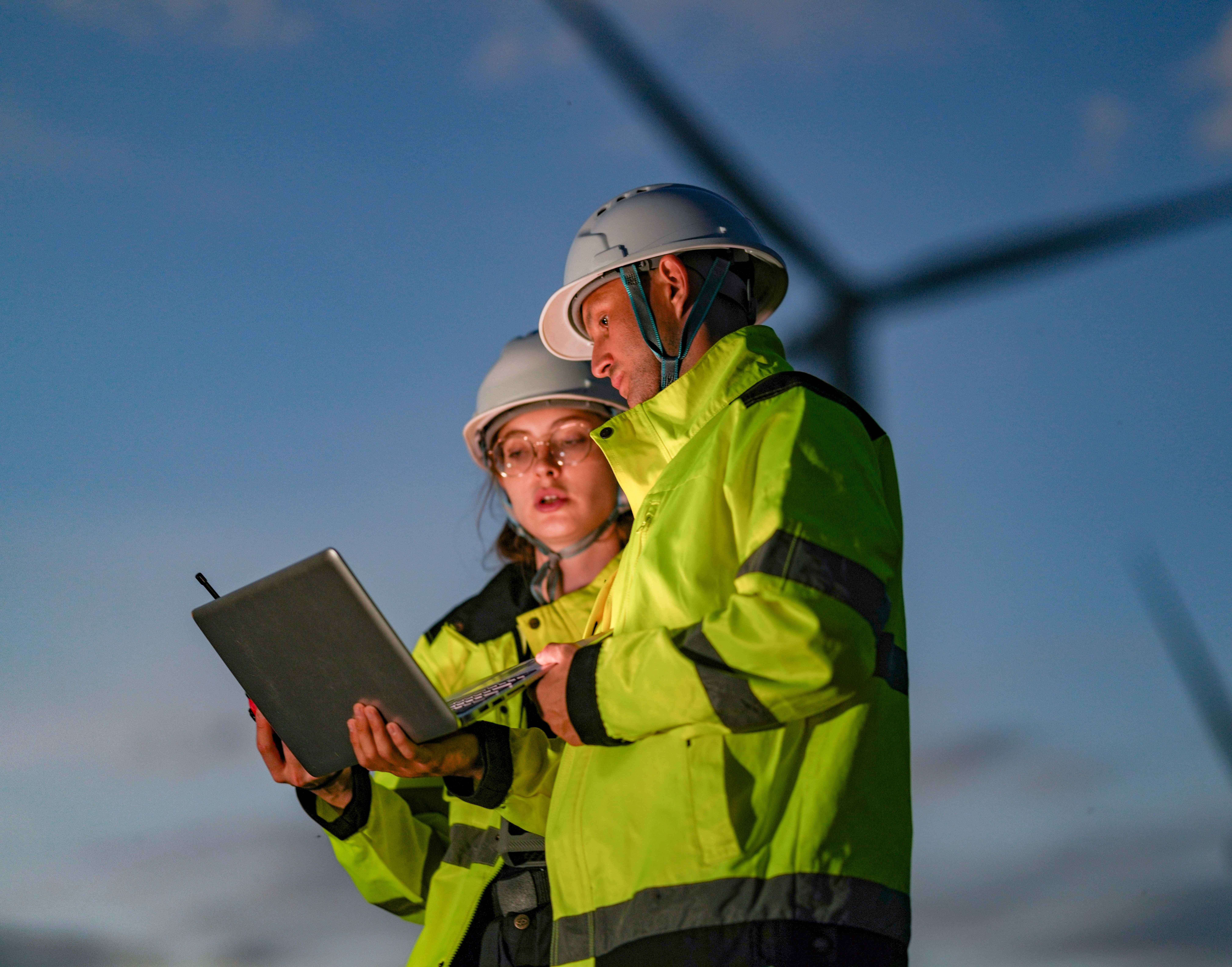 Two Exyte employees on a project with a windfarm in the background