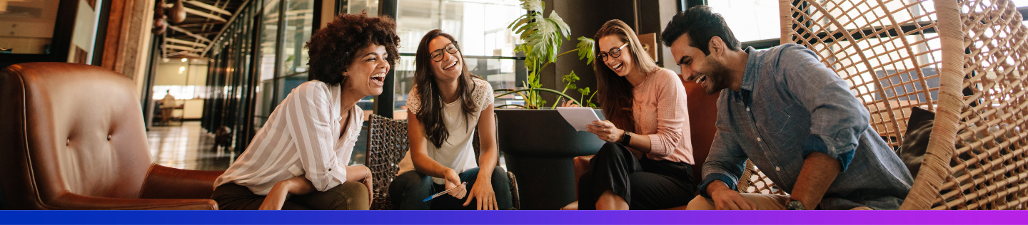 A diverse group of four young colleagues laughs together in a modern office lounge