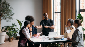 A diverse group of five colleagues collaborates in a bright, modern meeting room filled with plants.