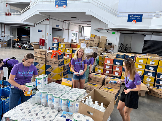 Alt Text: Three Franklin Templeton employees packing boxes with supplies during a relief effort in a warehouse setting.