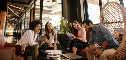 A diverse group of four young colleagues laughs together in a modern office lounge