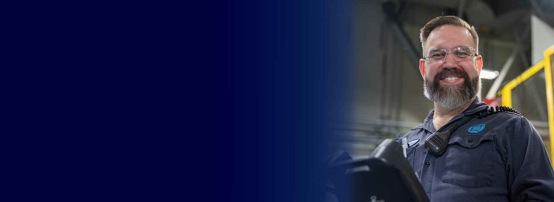 A GE Aerospace employee wearing a uniform with the GE logo and a communication device on their shoulder, standing in an industrial setting with machinery and equipment in the background. The left side of the image features a gradient blue overlay.