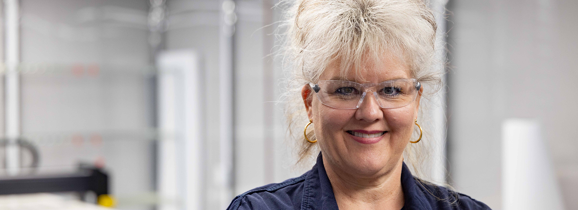 Woman with safety glasses on smiling at camera.