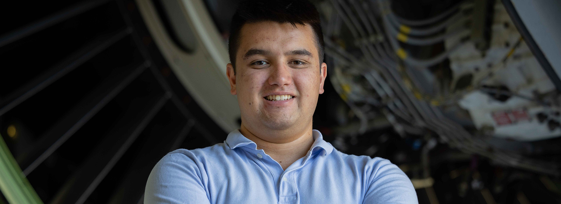 Young man with arms crossed standing in front of airplane engine.