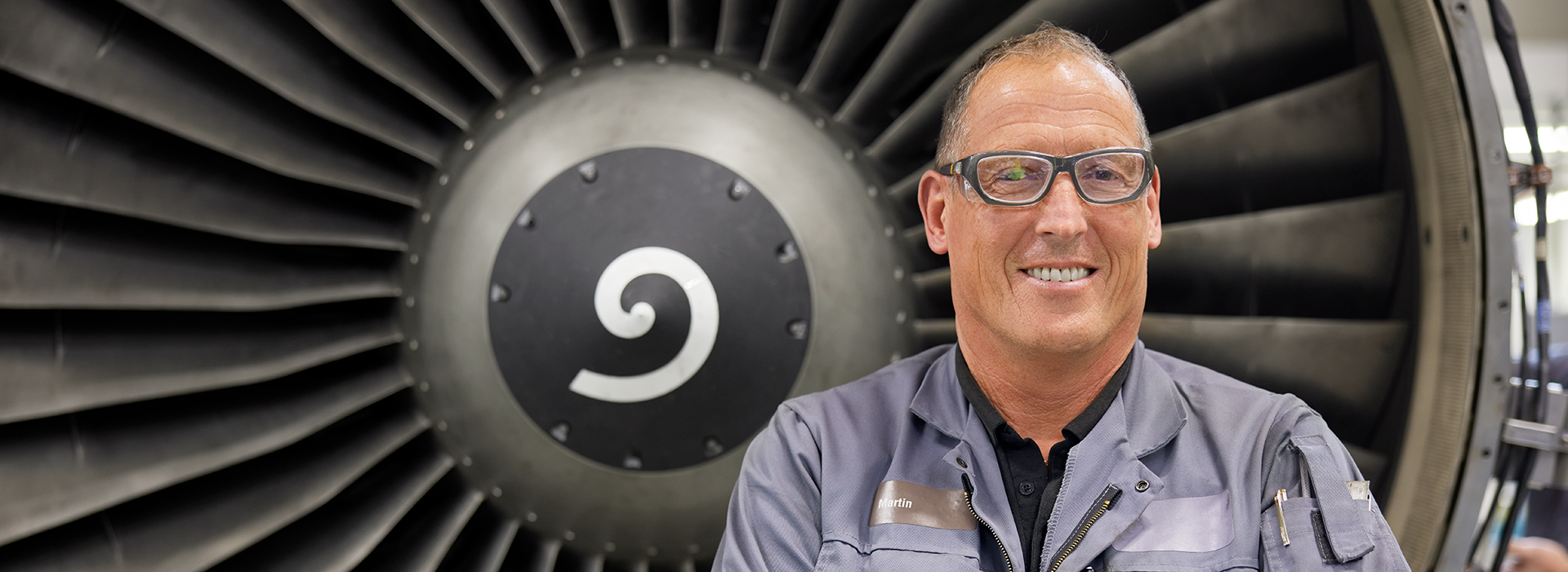 Wales male employee standing in front of jet engine.