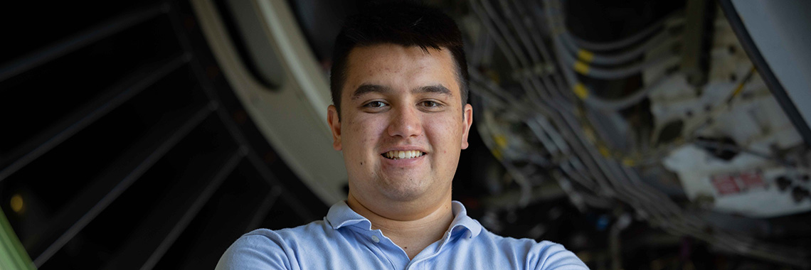 Young man with arms crossed standing in front of airplane engine.