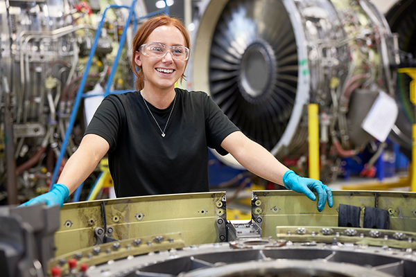 Female employee smiling while standing next to jet engine.