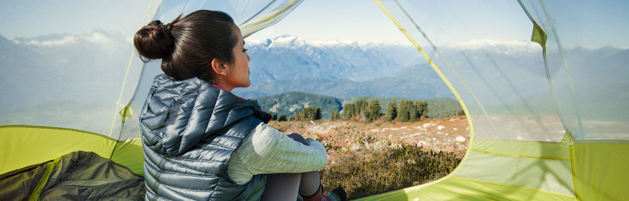 A woman looks at a view of mountains from inside a tent
