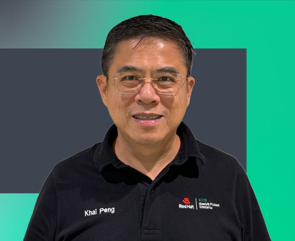 A man wearing glasses and a black polo shirt with "Khai Peng" and company logos stands in front of a teal and dark gray background, smiling at the camera.