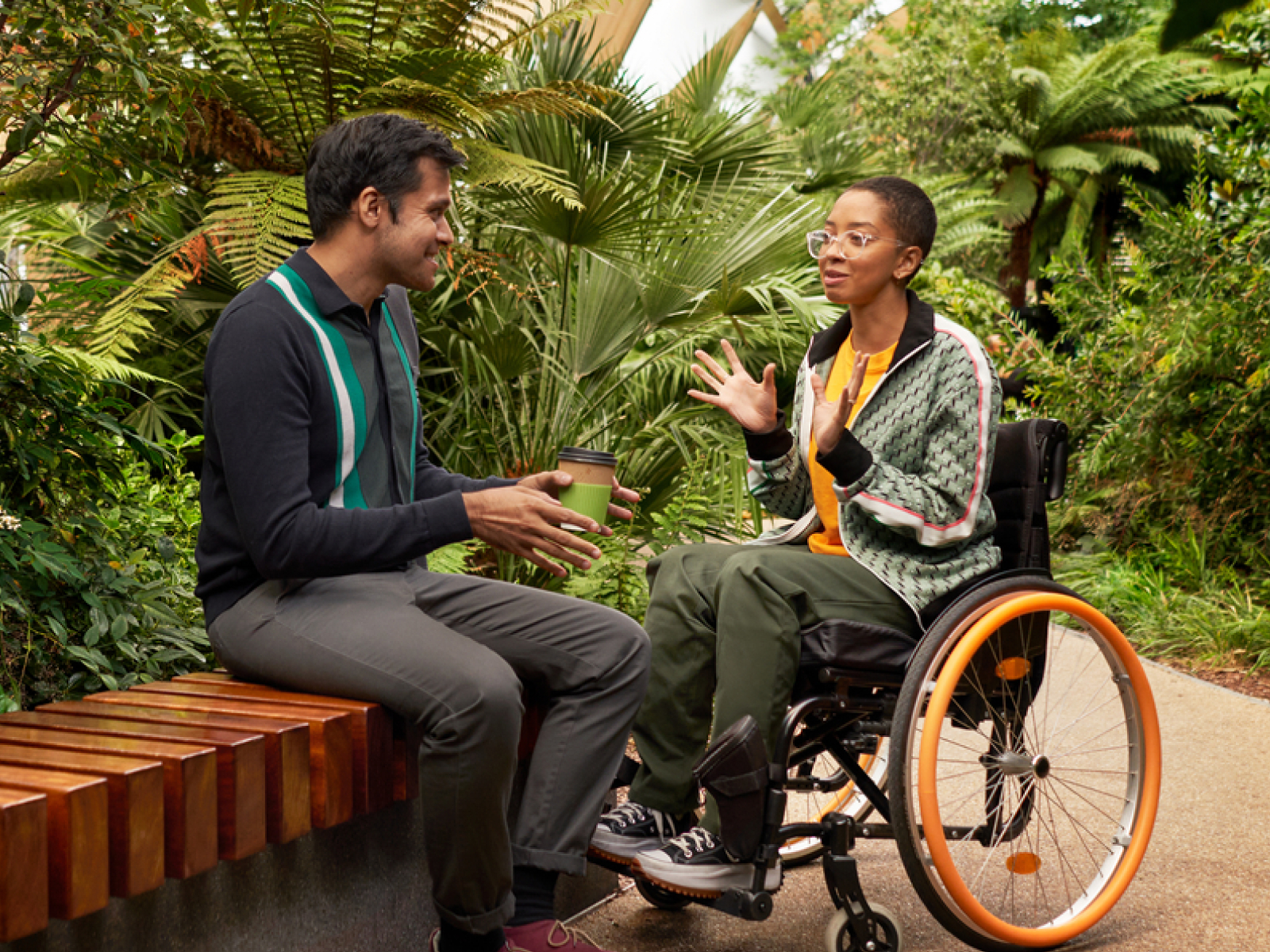 Young man on a bench talking to a young woman in a wheelchair surrounded by plants