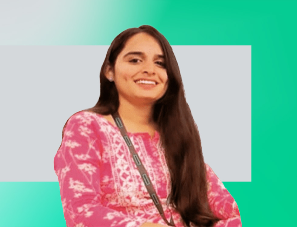 A woman with long dark hair, wearing a pink and white patterned top and a lanyard, is smiling against a light gray and teal-green background.