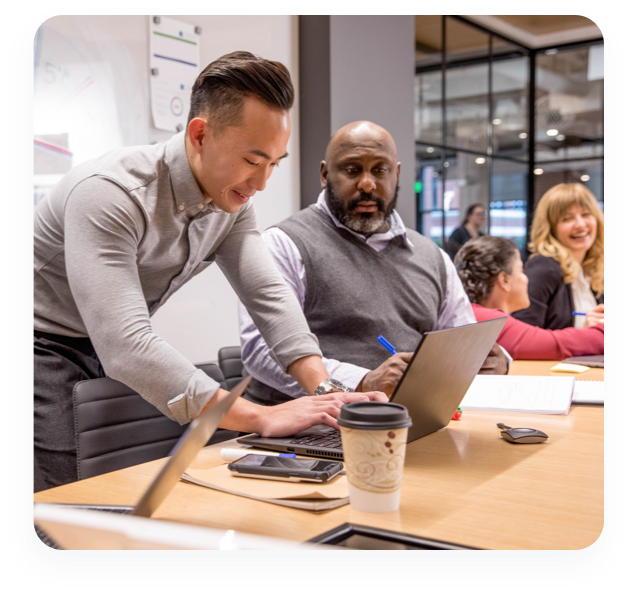 A group of men and women at a conference table at work collaborate with each other.