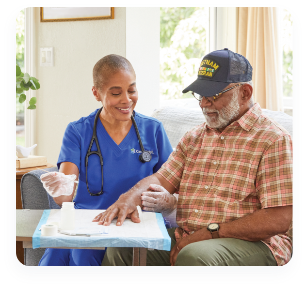 Nurse sitting cleaning and dressing an older man's wound on the couch in his home.