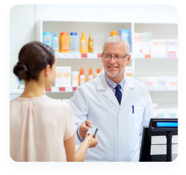 A CenterWell pharmacist talks to a woman customer at the pharmacy counter while handing her medication.