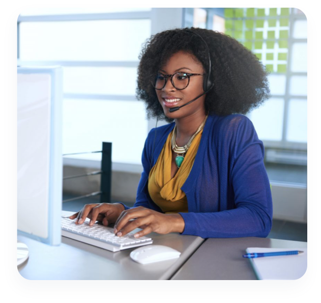 A smiling woman talks through her headset while sitting at a desk typing on her computer.