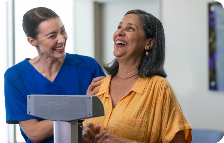 A medical assistant smiling with a happy female patient while being weighed during an office visit.