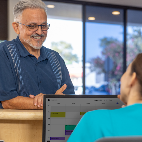 A senior male checks in at the front desk with a person behind a computer screen.