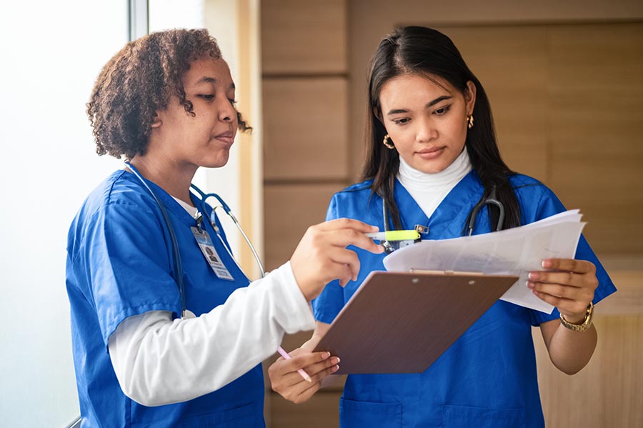 Two young females in scrubs reviewing medical records on a clipboard