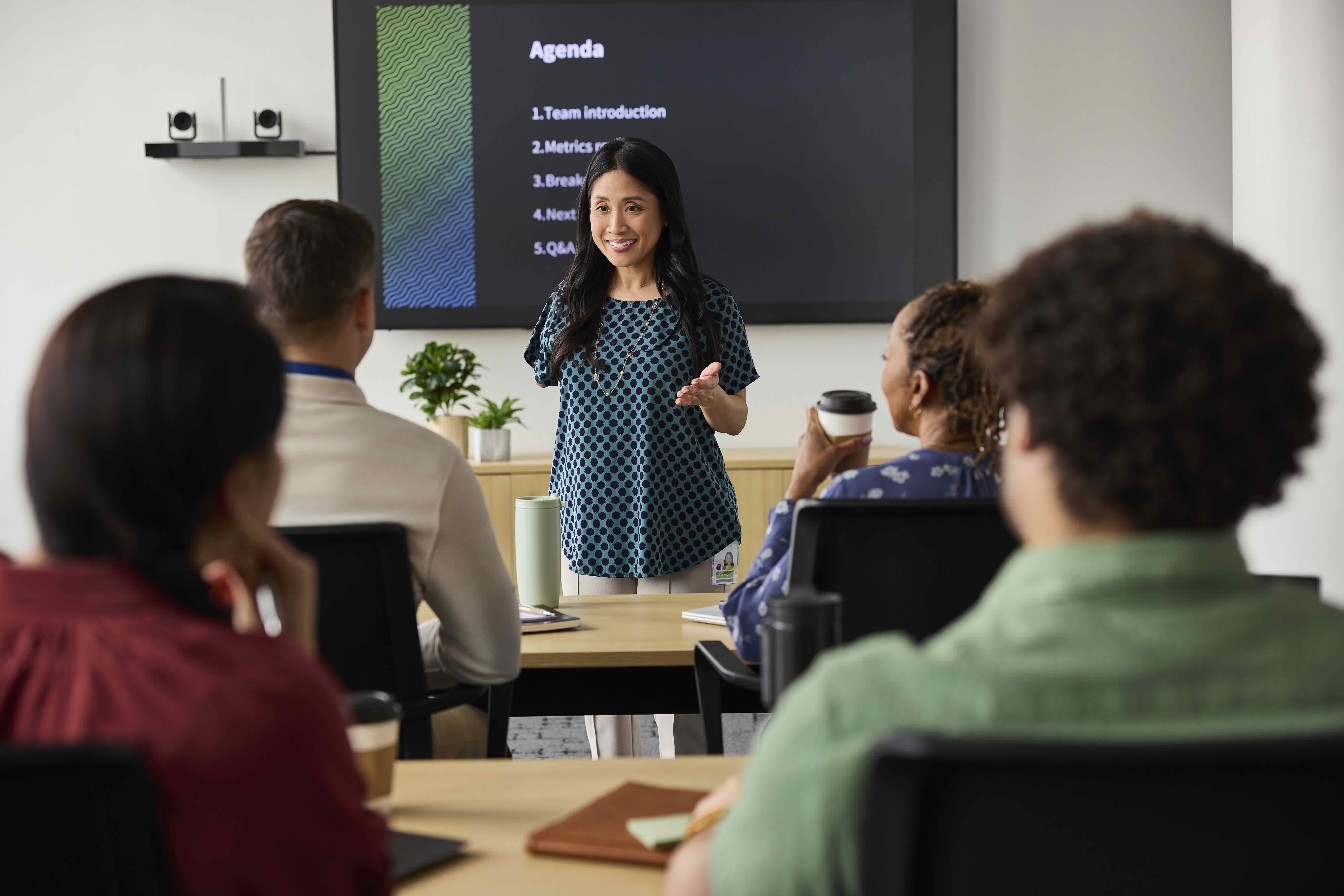 Holding in large person/virtual meeting in meeting room, presenting, townhall style.