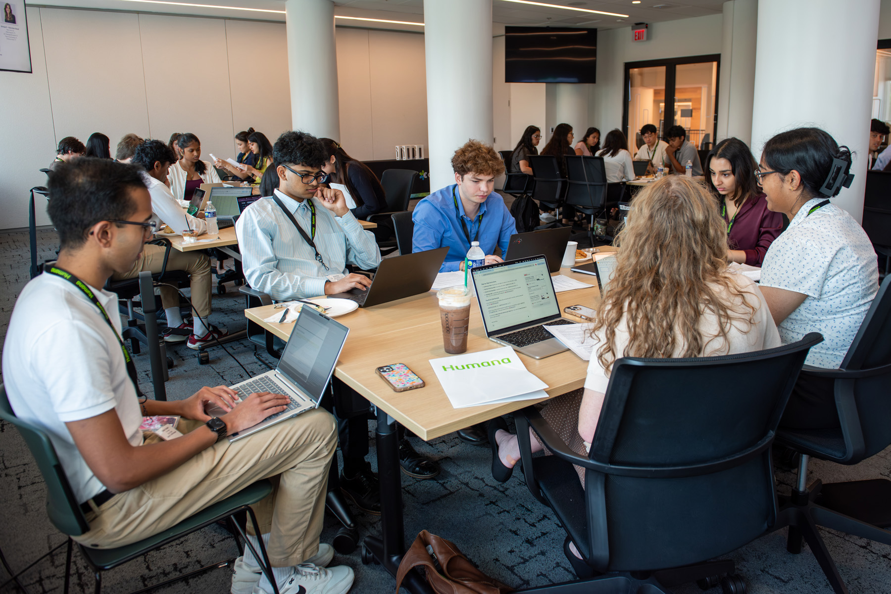 Group of Humana interns in large conference room working in small groups collaborating on a project