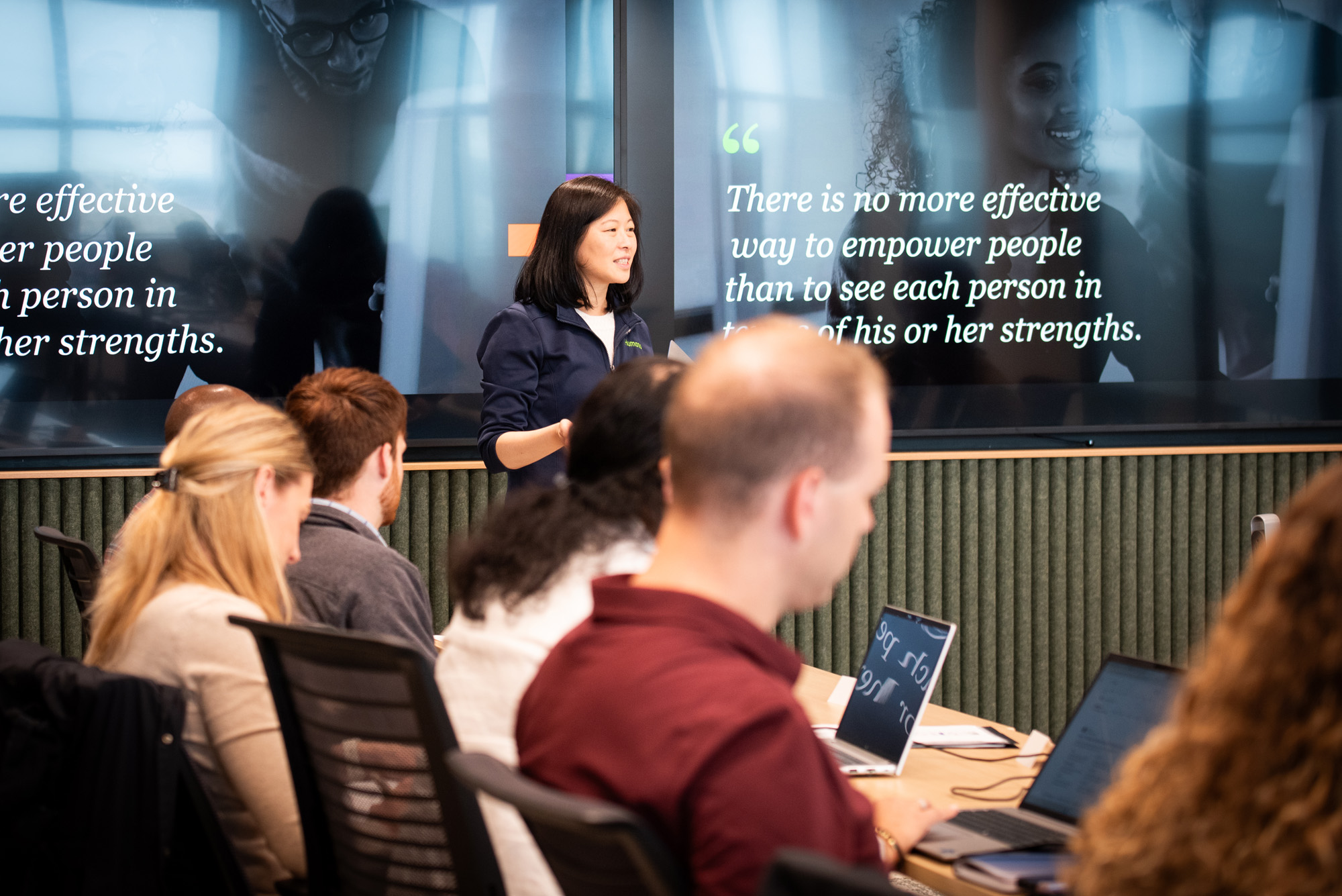 Asian women standing in front of a screen presenting to a room of students 