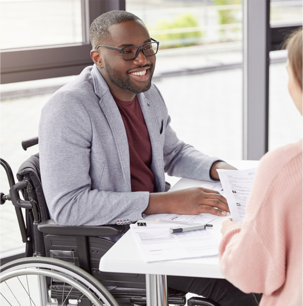 A man in a wheelchair smiling while meeting with another person in an office.