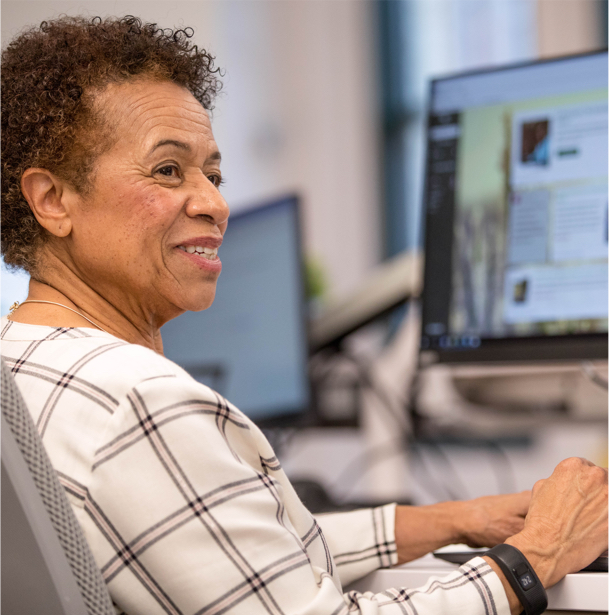 An older woman working at a computer while looking away smiling. 