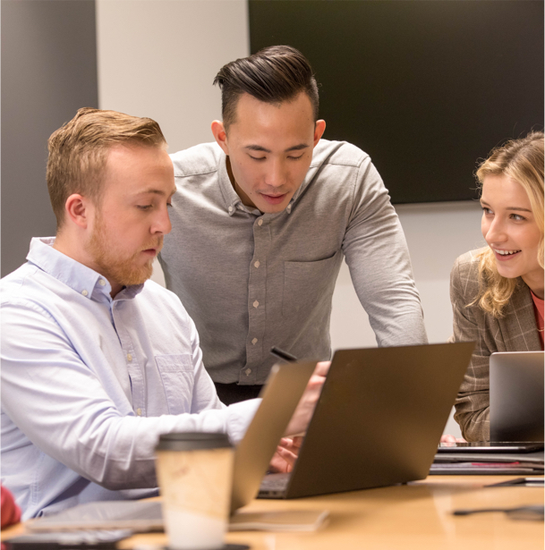 Three students gathered around a laptop in a conference room.